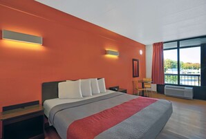 Habitación de hotel con una cama grande, dos mesitas de noche, un escritorio y una silla. Hay dos luces fijadas a la pared y una ventana con cortinas.