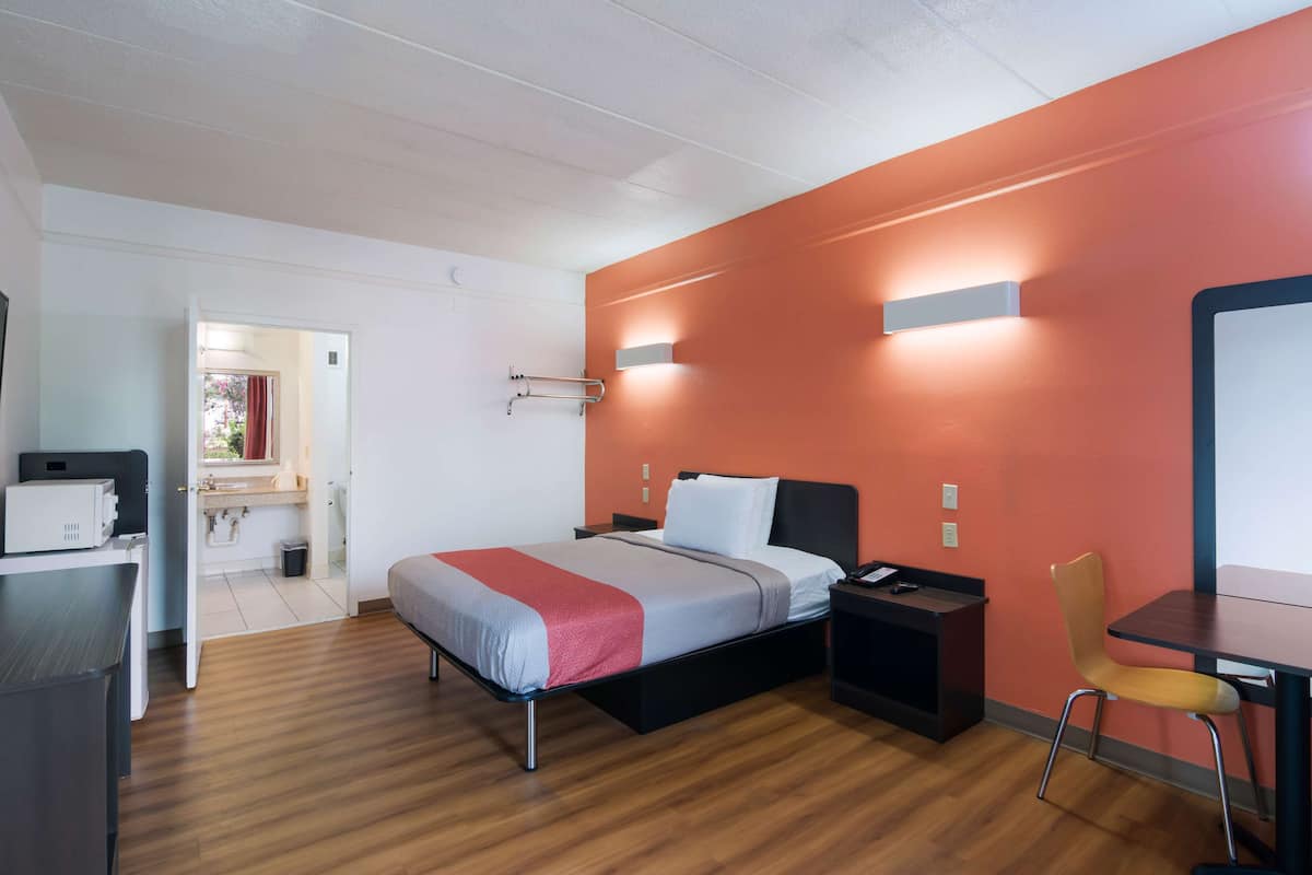 A modern hotel room with a bed, bedside table, chair, and a desk with a computer.