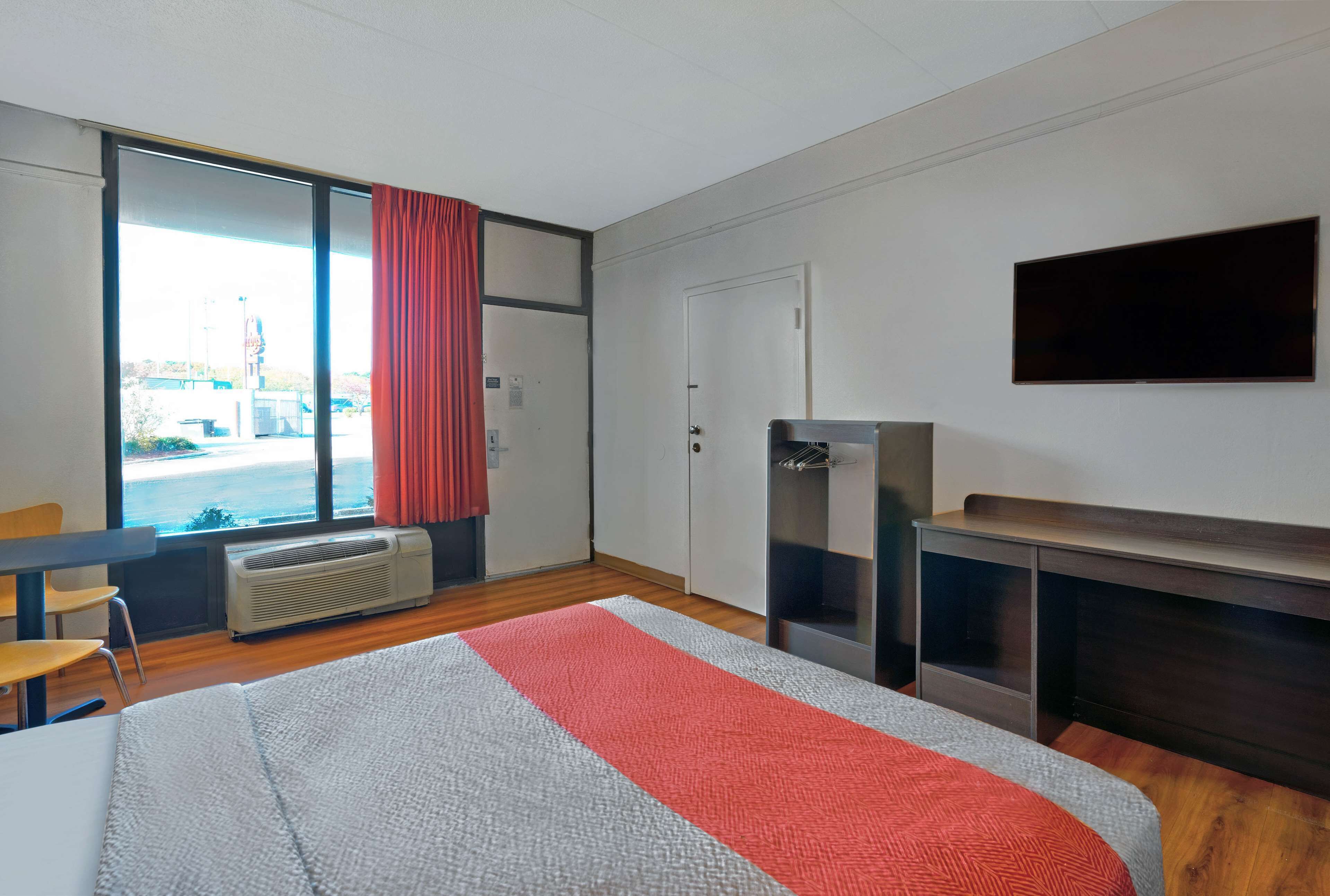 A hotel room with a bed, a desk, a TV, a heater, and a window with a view of the outside.