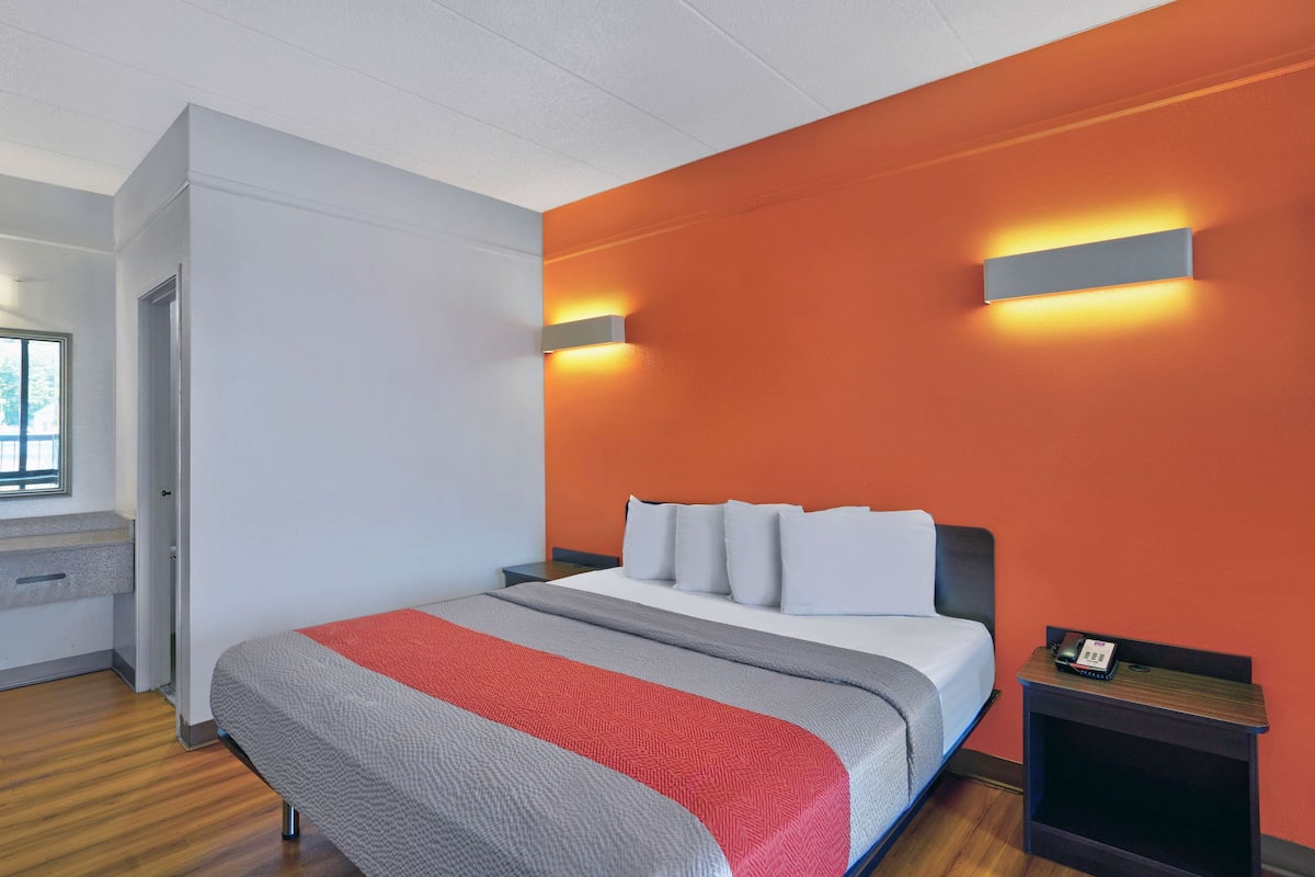 A modern hotel room with a bed, a nightstand, and a window.