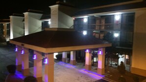 A gazebo with illuminated pillars, a tiled floor, and a building with multiple windows in the background. - Motel 6 Seaford, DE (Seaford)