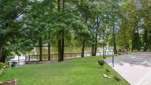 Un parque con un lago, árboles, un sendero pavimentado y una cerca.