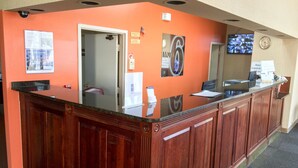 A reception desk with a glass top, wooden paneling, and a clock on the wall. - Motel 6 Seaford, DE (Seaford)