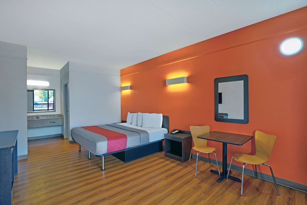 A hotel room with a bed, a desk, two chairs, a small table, and a mirror on the wall.