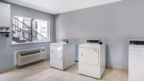 A laundry room with three stacked washers and dryers, a window with a view of a building, and a wall-mounted heater. - Econo Lodge Inn & Suites Virginia Beach - Norfolk (Virginia Beach)
