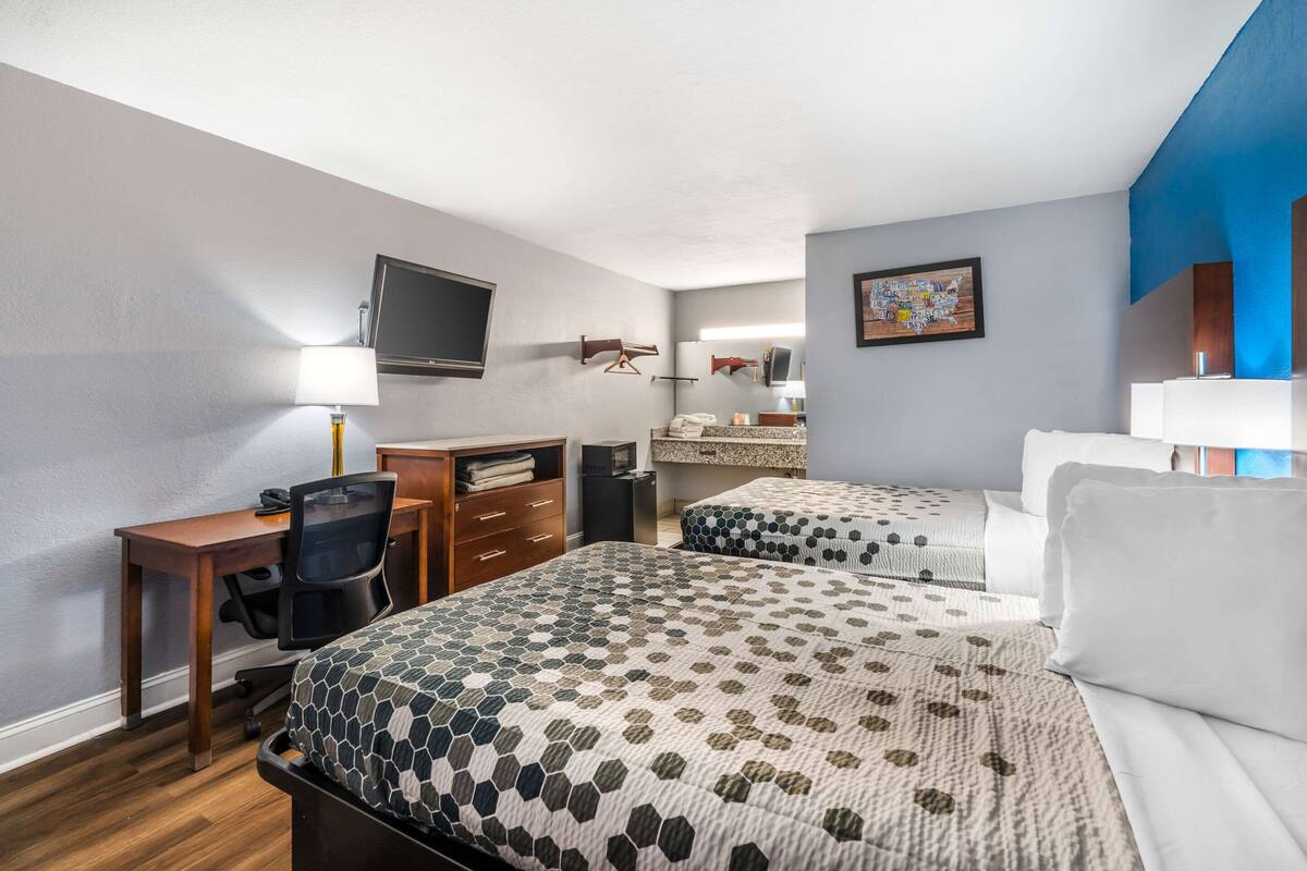 A hotel room with two beds, a desk, a chair, a TV, and a bathroom.