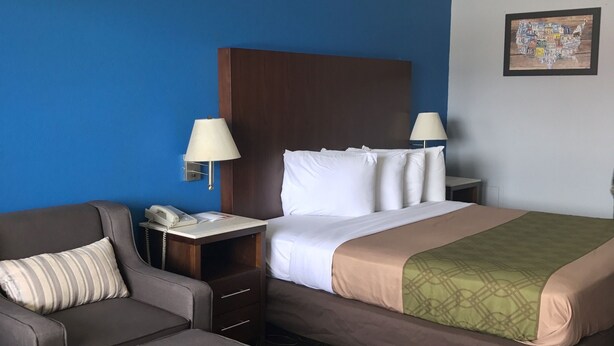 A hotel room with a bed, a chair, a nightstand, and a lamp. - Econo Lodge Inn & Suites Virginia Beach - Norfolk (Virginia Beach)