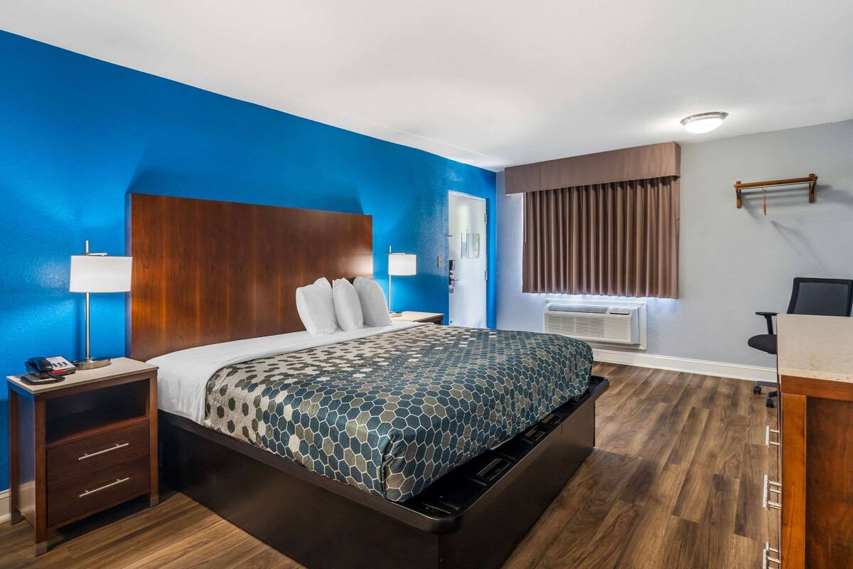 A hotel room with a bed, nightstand, lamp, and a window with curtains.
