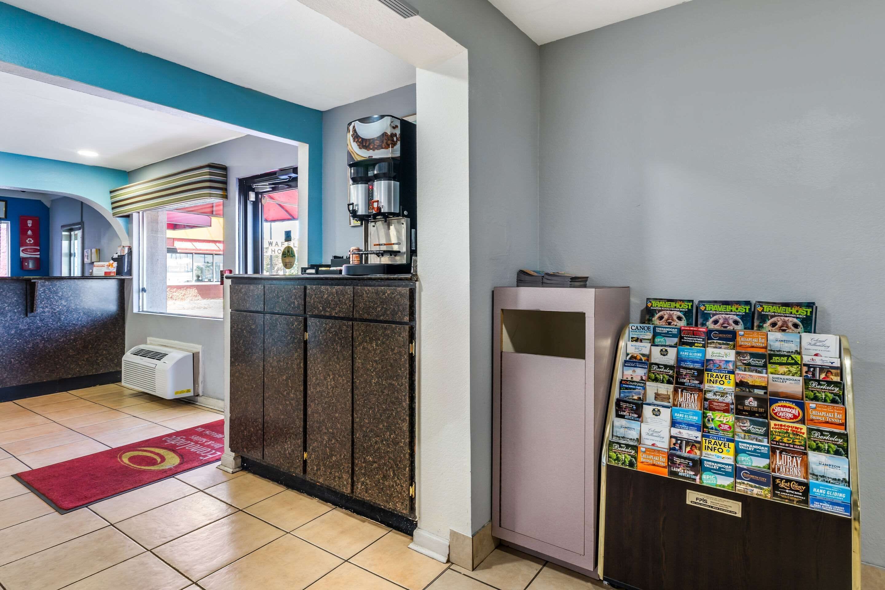 Un vestíbulo de hotel con mostrador de recepción, máquina de café, refrigerador con folletos turísticos y alfombra roja.