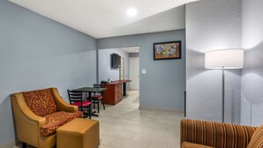 A living room with a sofa, ottoman, and armchair, a dining area with a table and chairs, and a kitchen area with a counter and cabinets. - Econo Lodge Inn & Suites Virginia Beach - Norfolk (Virginia Beach)