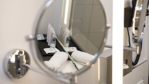 A bathroom mirror reflecting a towel rack with towels, a bottle, and a tissue box. - Mercure Hotel Mannheim am Friedensplatz (Mannheim)
