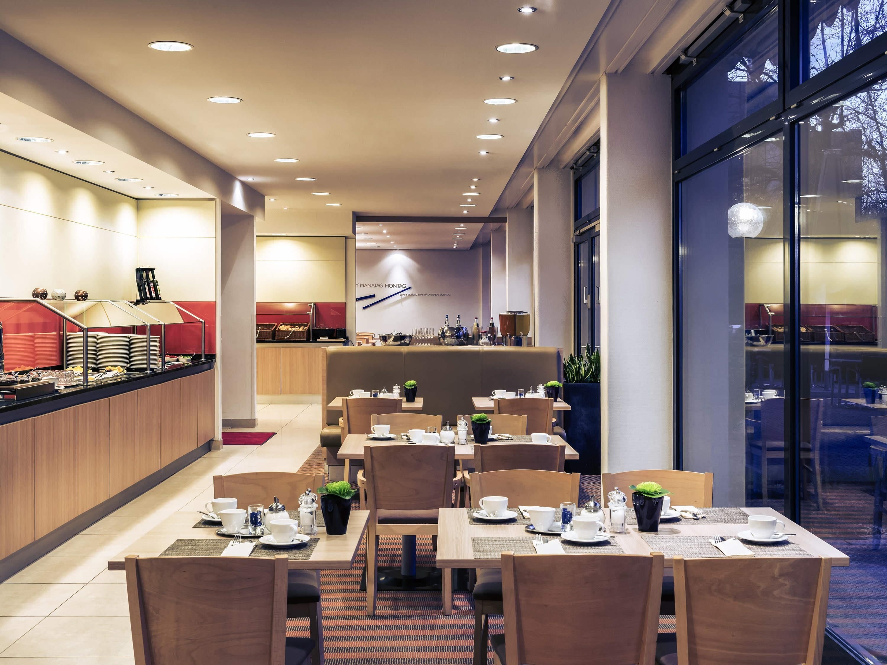 Un moderno comedor con varias mesas y sillas, un mostrador de buffet y un amplio ventanal que ofrece vistas al exterior.