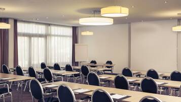 Una sala de conferències amb diverses taules i cadires, una pissarra i il·luminació penjant.