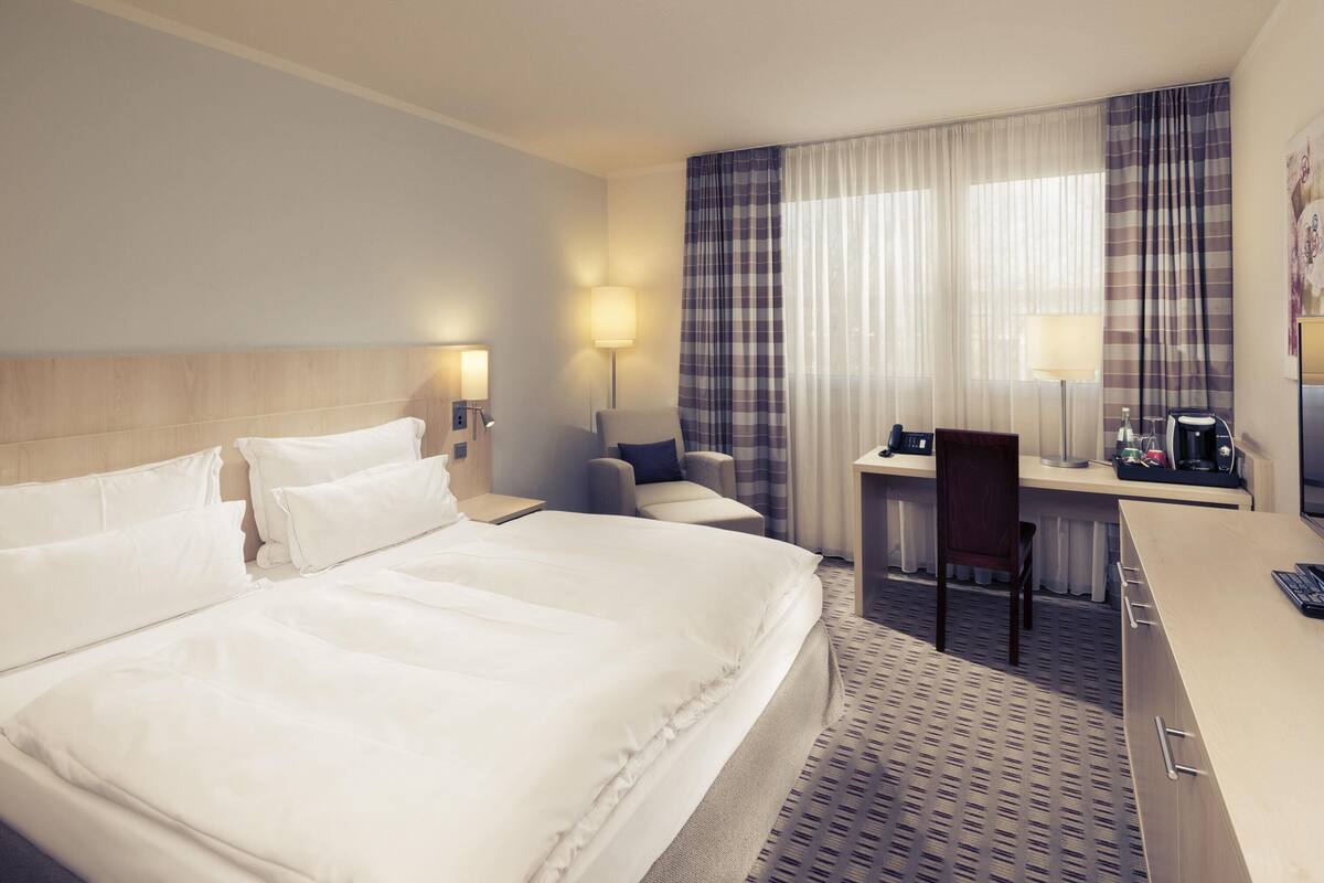 Una habitación de hotel con una cama grande, un escritorio, una silla y una lámpara de escritorio.