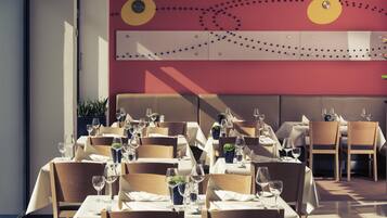 Un restaurant où les tables sont dressées pour le service, avec un décor intérieur moderne caractérisé par un mur d’accent rouge et des éléments décoratifs au plafond.