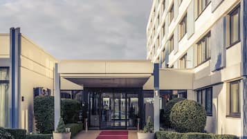 A modern hotel entrance with a covered walkway, glass doors, and a red carpet.