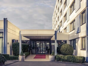 Entrada d'un hotel modern amb una passarel·la coberta, portes de vidre i catifa vermella.