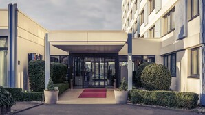 Une entrée d’hôtel moderne avec une allée couverte, des portes en verre et un tapis rouge.