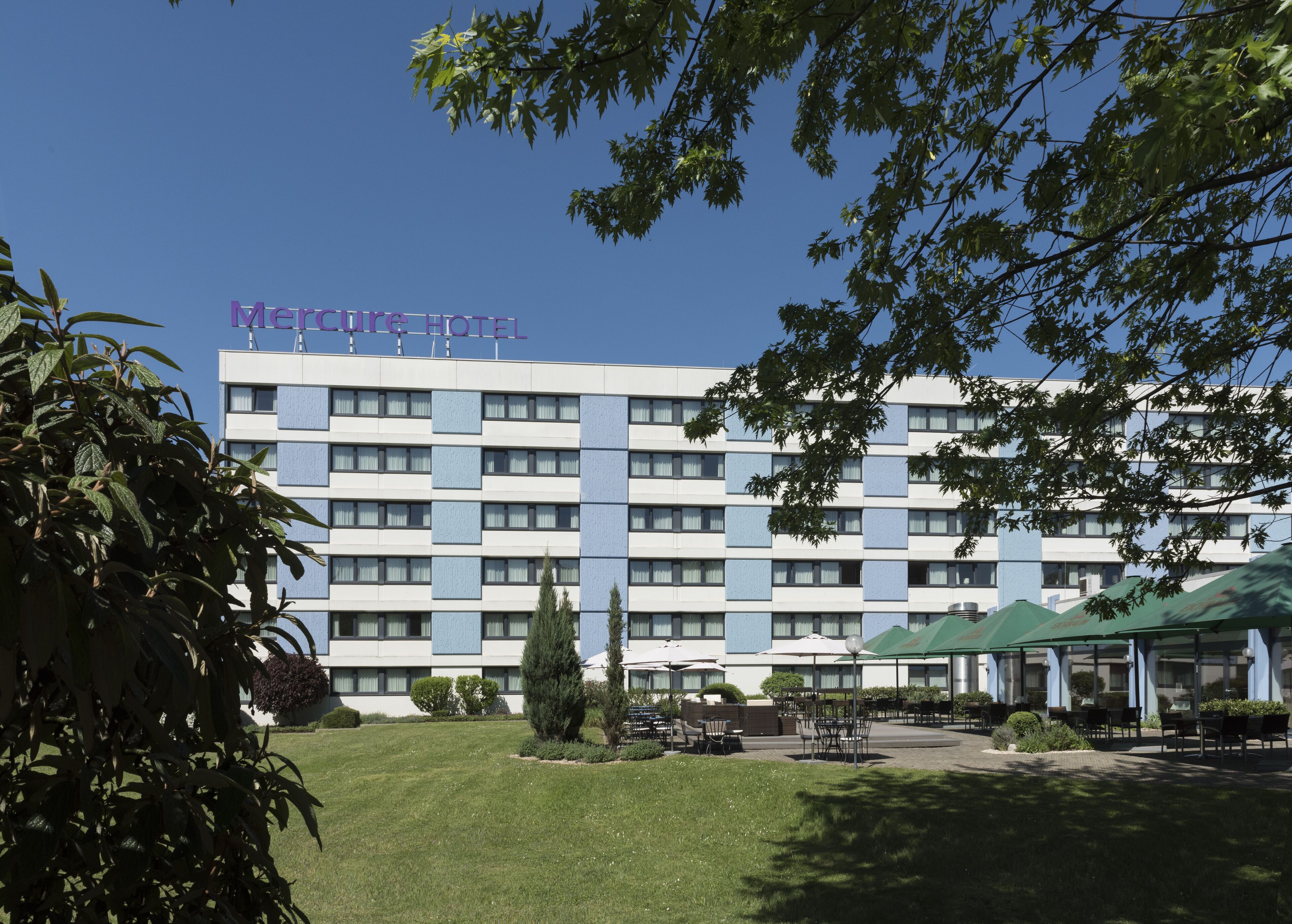 Un hôtel au design moderne, doté d’un toit plat et d’un grand espace extérieur aménagé avec des parasols.