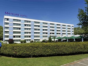 Un hotel de varios pisos con fachada moderna, un cartel que dice 'Mercure Hotel' y un césped cuidado con un seto delantero.