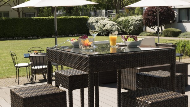 Un espace extérieur aménagé pour les repas, avec des meubles en osier, une table en verre et des parasols.