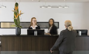 Un mostrador de recepción con una planta en maceta, una pantalla digital y una obra de arte enmarcada en la pared.
