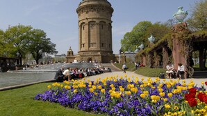 A historic tower with a dome, surrounded by a flower garden with yellow and purple flowers, and a paved walkway. - Mercure Hotel Mannheim am Friedensplatz (Mannheim)