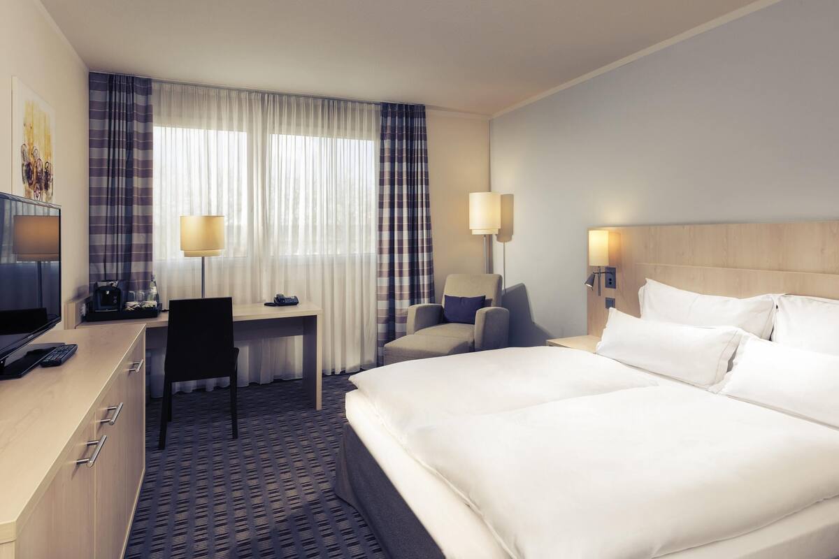 Una habitación de hotel con cama, escritorio, silla y dos lámparas de noche.
