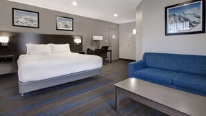 A hotel room with a bed, a blue sofa, a desk, and a lamp.