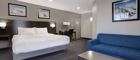 A hotel room with a bed, a blue sofa, a desk, and a lamp.