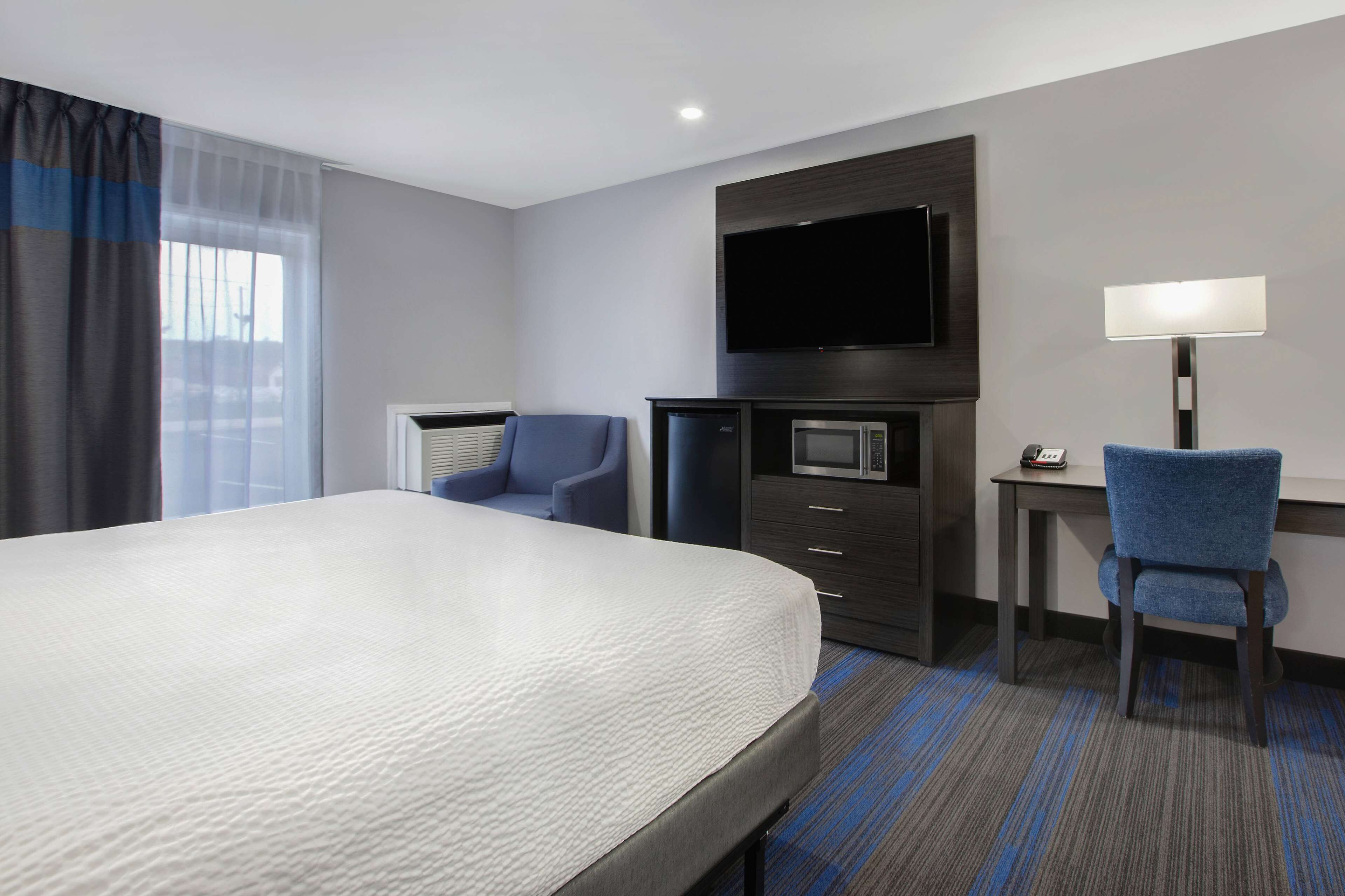Habitación de hotel con una cama grande, un escritorio con silla, un televisor de pantalla plana en la pared y un microondas.