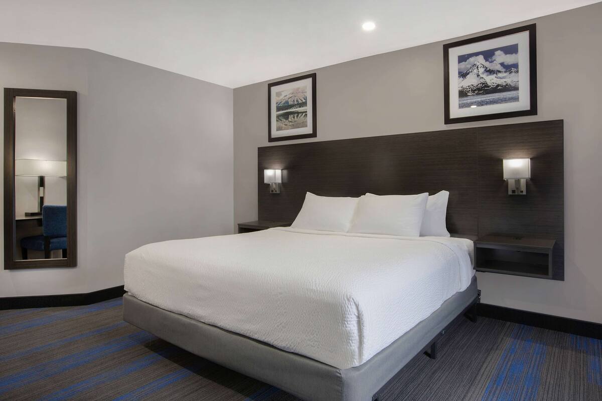 A hotel room with a large bed, two wall-mounted lamps, a framed picture on the wall, and a mirror on the left.