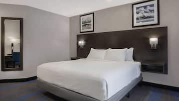 A hotel room with a large bed, two wall-mounted lamps, a framed picture on the wall, and a mirror on the left.