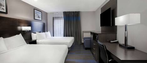 Habitación de hotel con dos camas, un escritorio, una silla, un televisor y una ventana con cortinas.