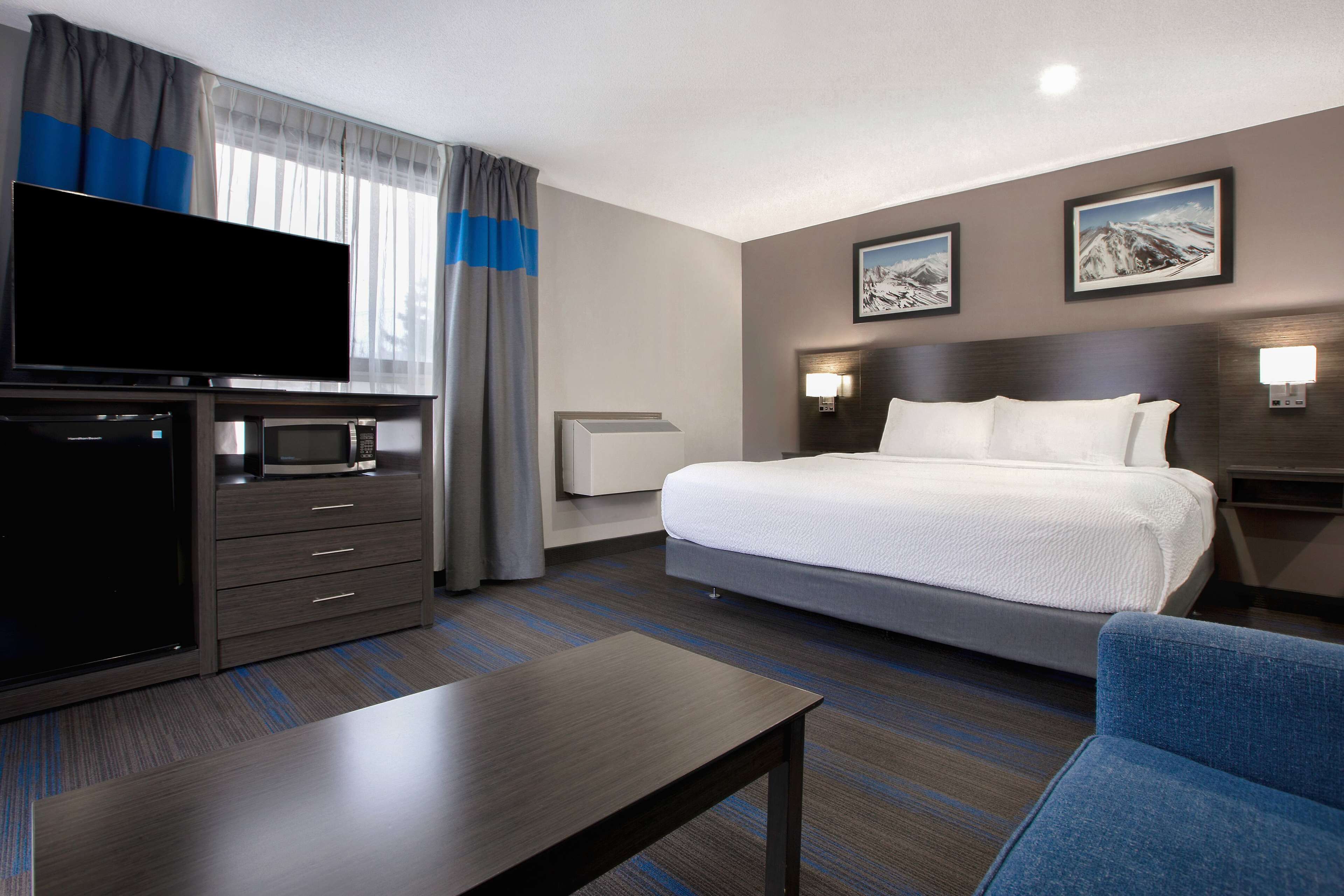 A hotel room with a bed, a flat-screen TV, a microwave, a coffee maker, a desk, and a chair.
