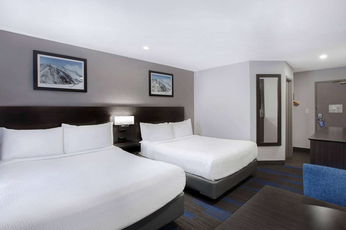 A hotel room with two beds, a desk, a chair, and two framed pictures on the wall.