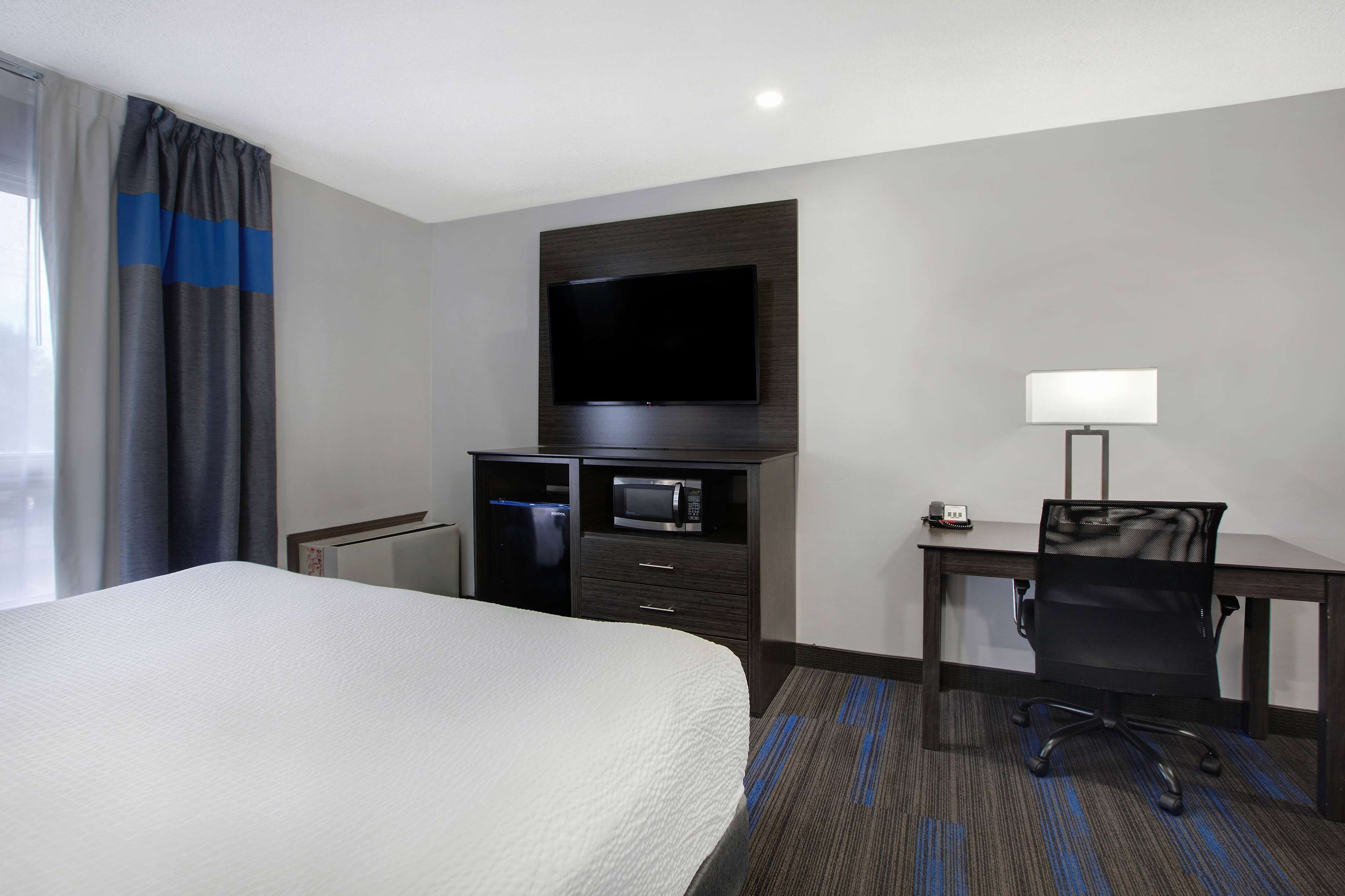 Une chambre d’hôtel dotée d’un grand lit, d’un téléviseur à écran plat fixé au mur, d’un bureau avec une chaise, d’un four à micro-ondes et d’une lampe.
