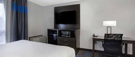 Une chambre d’hôtel dotée d’un grand lit, d’un téléviseur à écran plat fixé au mur, d’un bureau avec une chaise, d’un four à micro-ondes et d’une lampe.