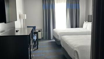 Une chambre d’hôtel équipée d’un téléviseur à écran plat, d’un bureau avec une lampe, de deux lits et d’une fenêtre avec des rideaux.