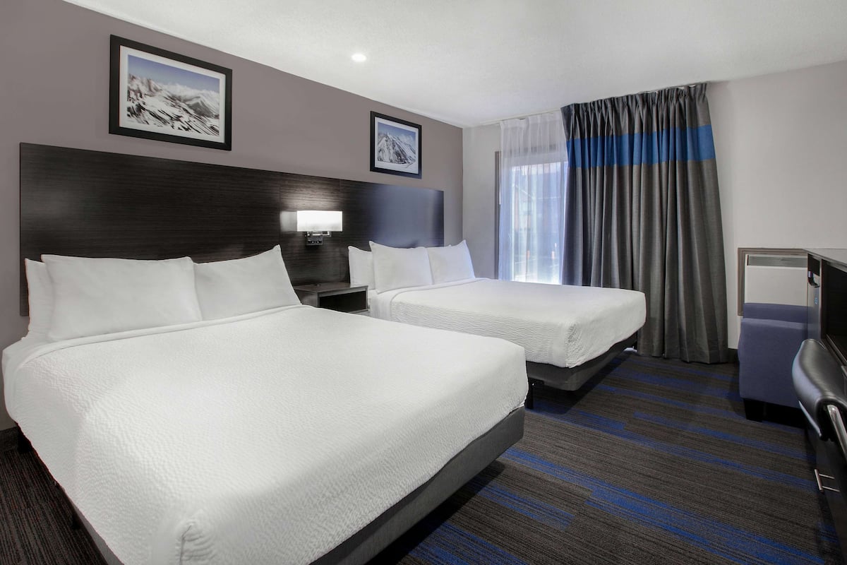 A hotel room with two beds, a desk, a chair, and a TV.