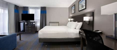 A hotel room with a bed, a desk, a chair, a television, and a desk lamp.