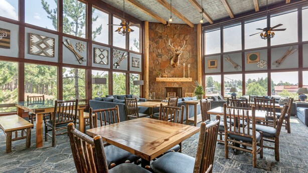 A rustic dining area with wooden tables and chairs, large windows, and a stone wall with a mounted deer head. - Comfort Inn Flagstaff South I-17 (Flagstaff)
