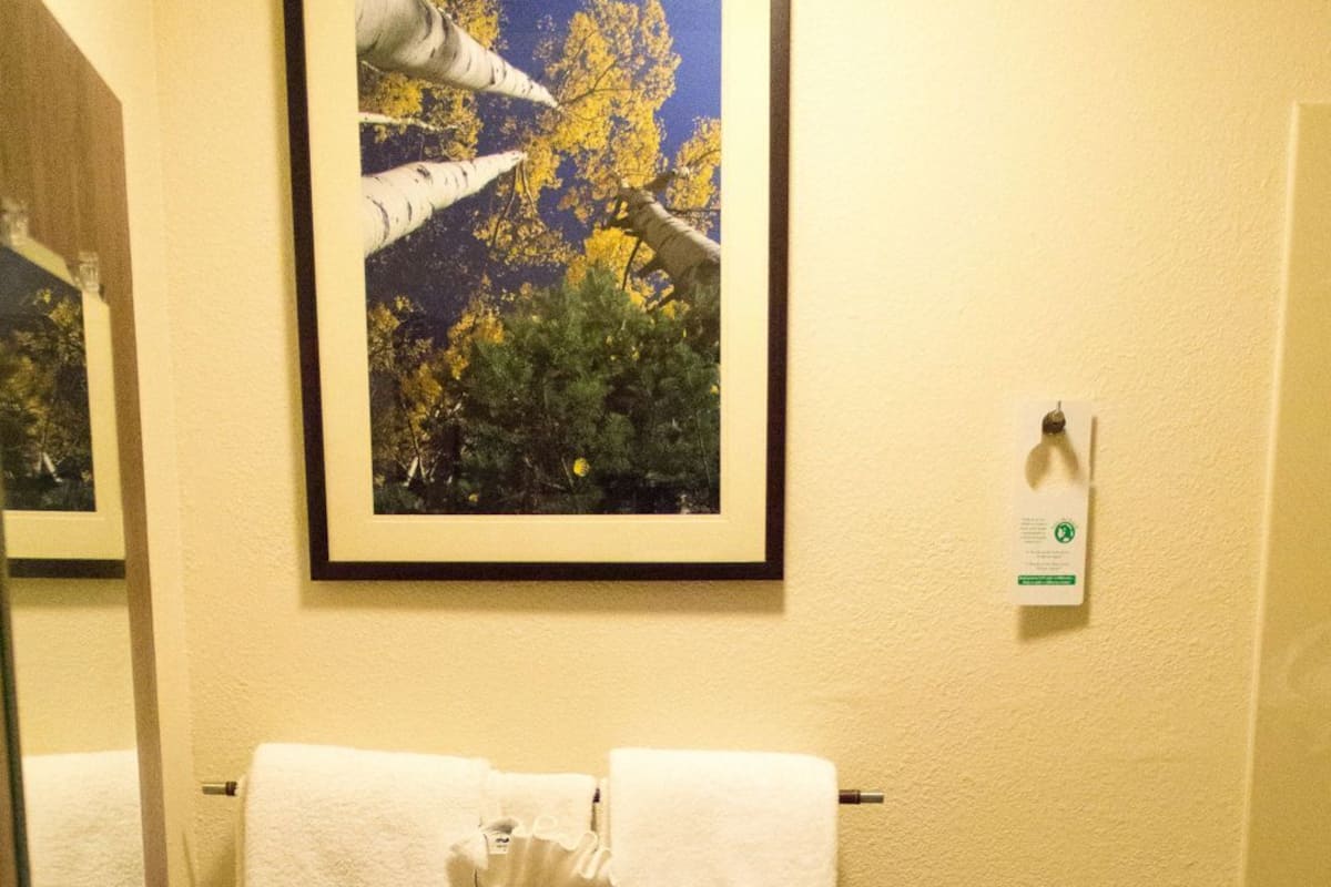 A bathroom with a toilet, two towels on the wall, and a framed picture above the toilet.