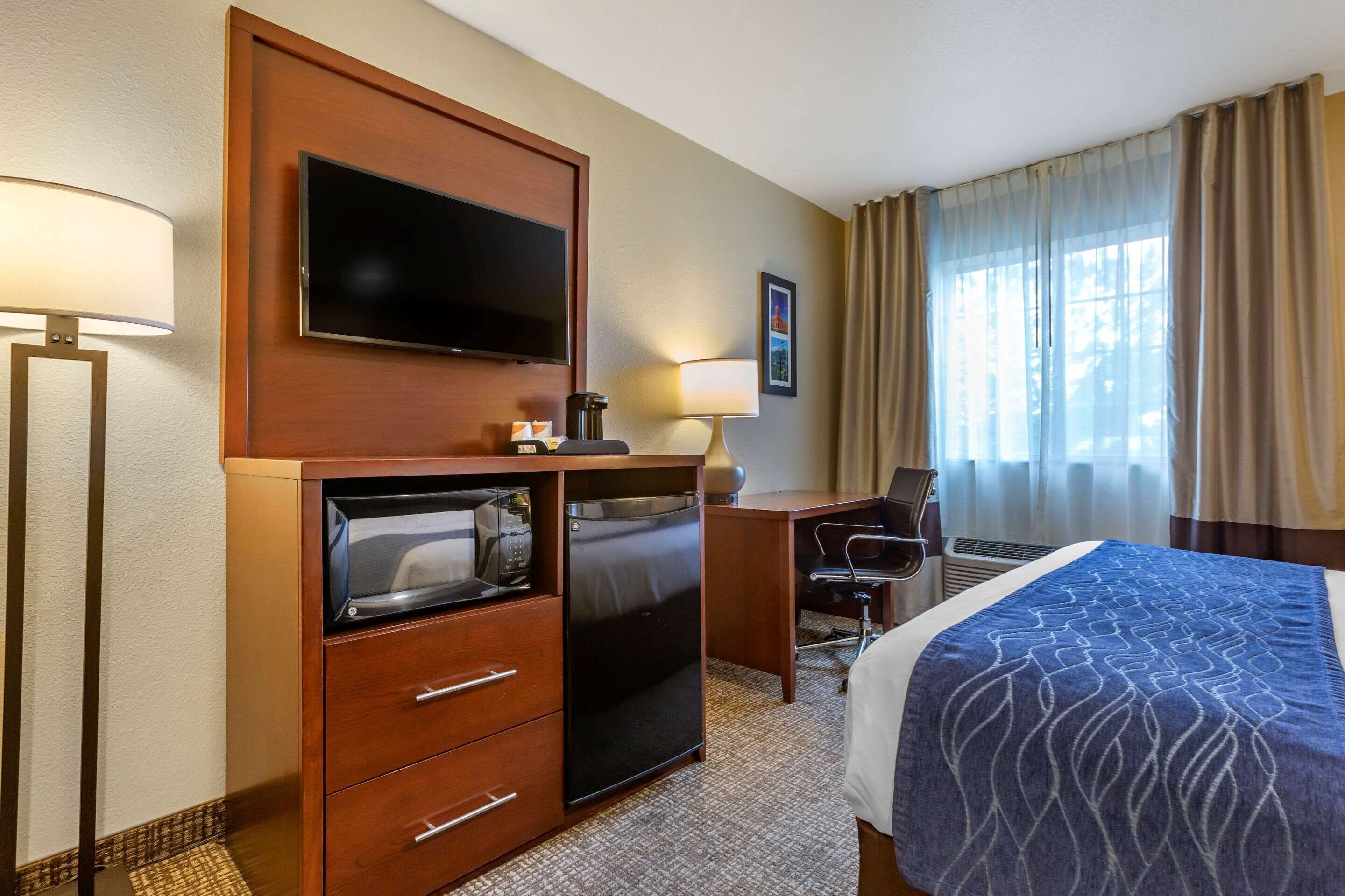 A hotel room with a bed, a desk, a television, a microwave, a coffee maker, and a window with curtains.