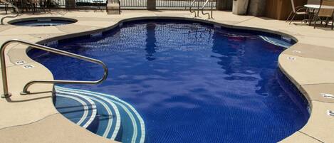 A swimming pool with a metal ladder, tiled deck, and outdoor seating area with chairs and tables.