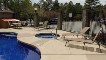 A pool area with lounge chairs, a hot tub, and a fenced parking area.