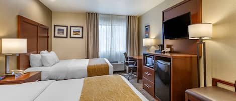 A hotel room with two beds, a desk, a television, and a chair.