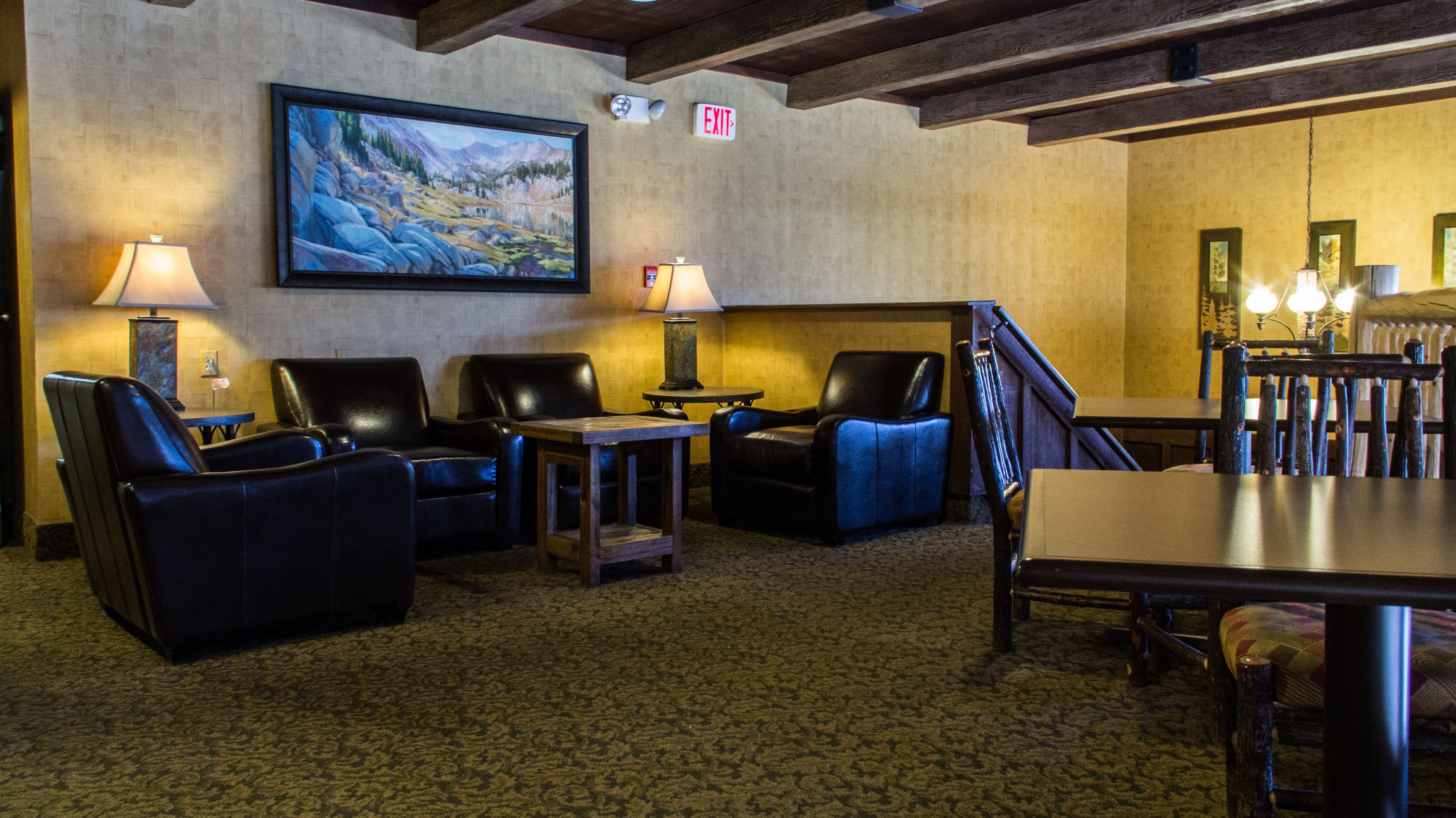 A lobby with leather chairs, a painting, and an exit sign.
