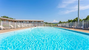Une piscine à l’eau d’un bleu cristallin, entourée d’une clôture blanche et de chaises longues.