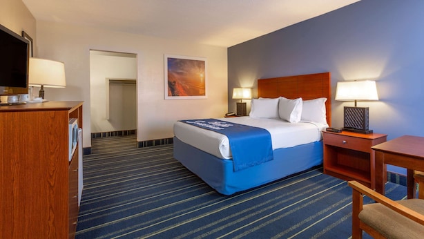Une chambre d’hôtel comprenant un lit, une table de chevet, une lampe, une télévision et un bureau avec une chaise.